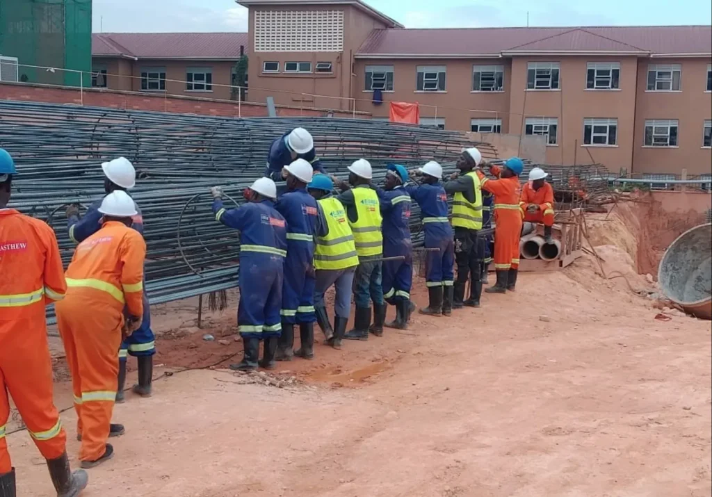 Site crew in helmets and overalls lifting a steel reinforcement cage
