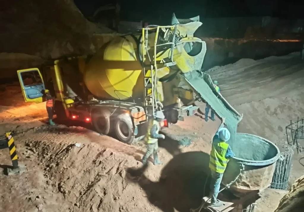Concrete mixer truck and workers pouring a foundation at night under lights