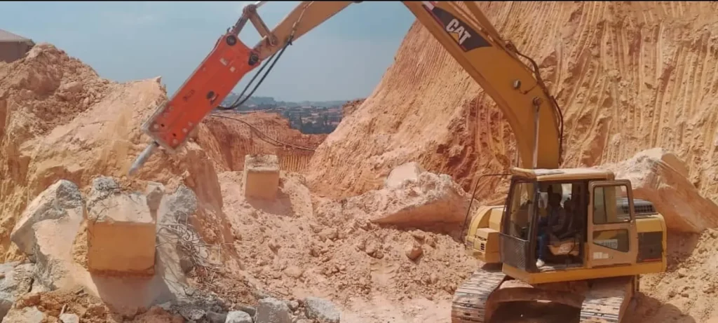 Excavator with a hydraulic rock breaker working on a rock face
