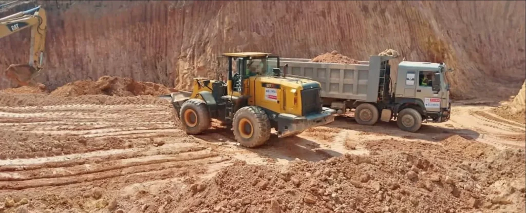 Wheel loader and tipper truck below a tall red earth cut face