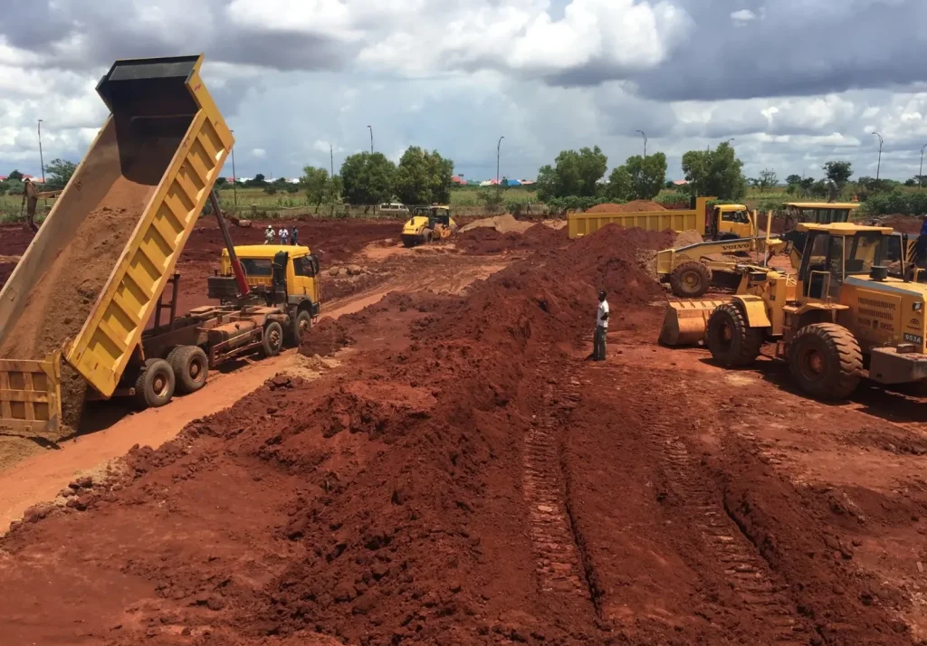Dump truck tipping soil while graders level a large site