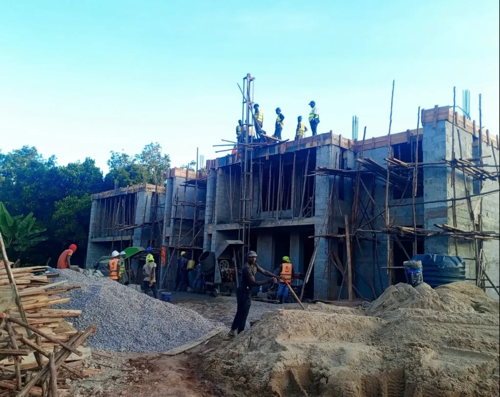 Multi-storey concrete frame under construction with workers on the upper deck and scaffolding
