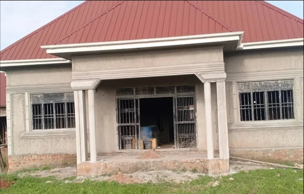 Front of a plastered bungalow with a columned porch and red iron-sheet roof