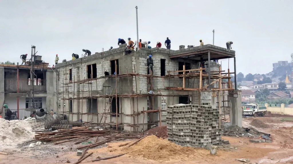Storeyed concrete block building under construction with workers on the top floor
