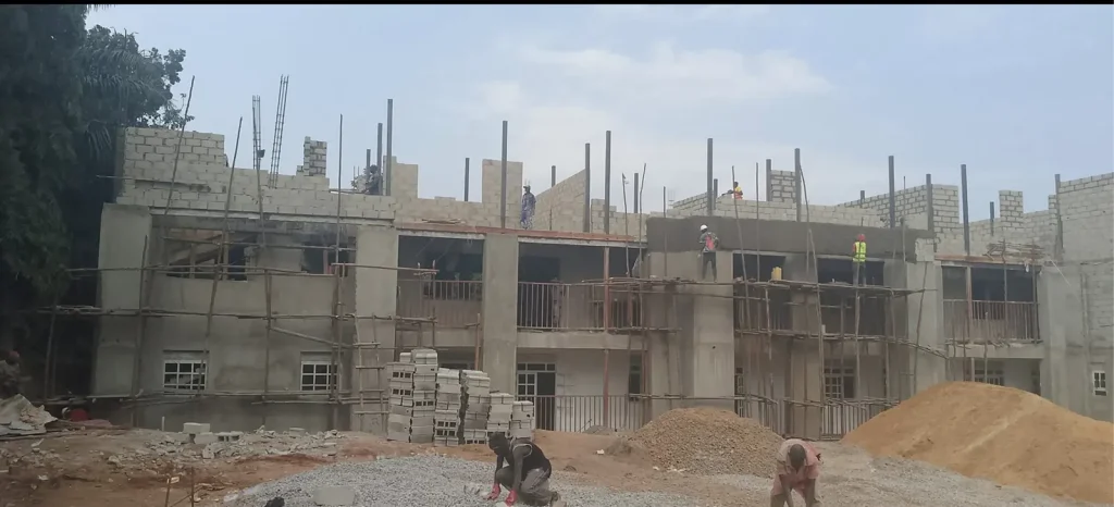 Two-storey block building under construction with scaffolding and steel bars rising from the top