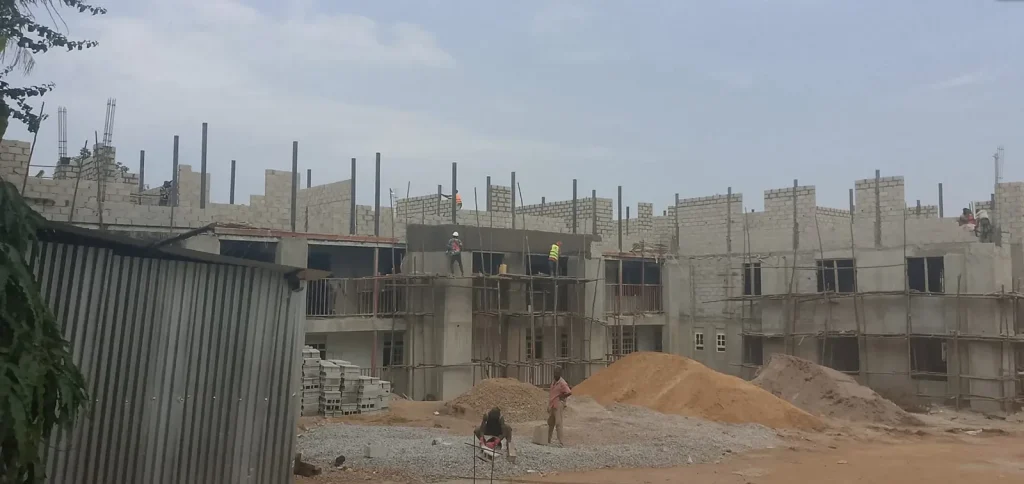 Long two-storey block structure with scaffolding seen from across the site