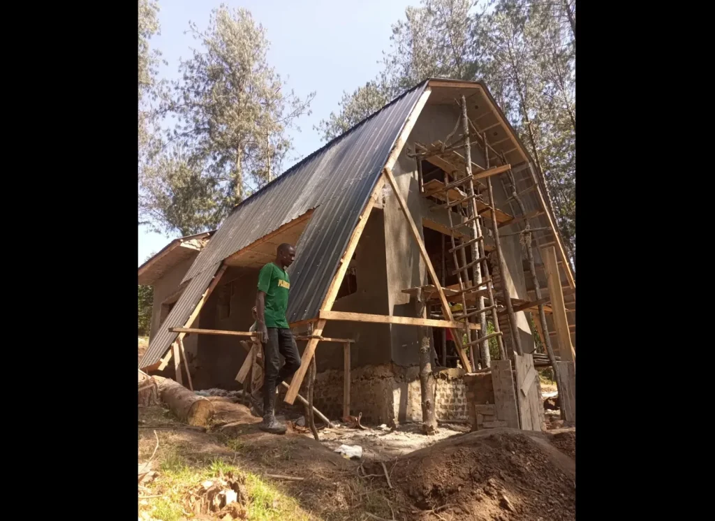 A-frame cabin under construction with a worker standing beside the timber frame